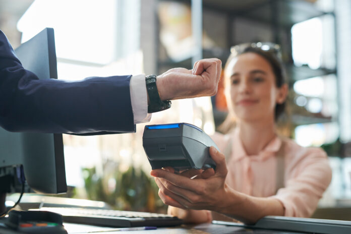 Man hält Smartwatch über ein Lesegerät und bezahlt in einem Geschäft|