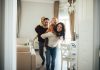 Altersvorsorge-Reform: Meldewesen als Erfolgsfaktor Happy parents playing energetically with their young children in a bright living room. Both parents carry their kids while laughing and moving around, capturing a joyful family moment full of motion and connection